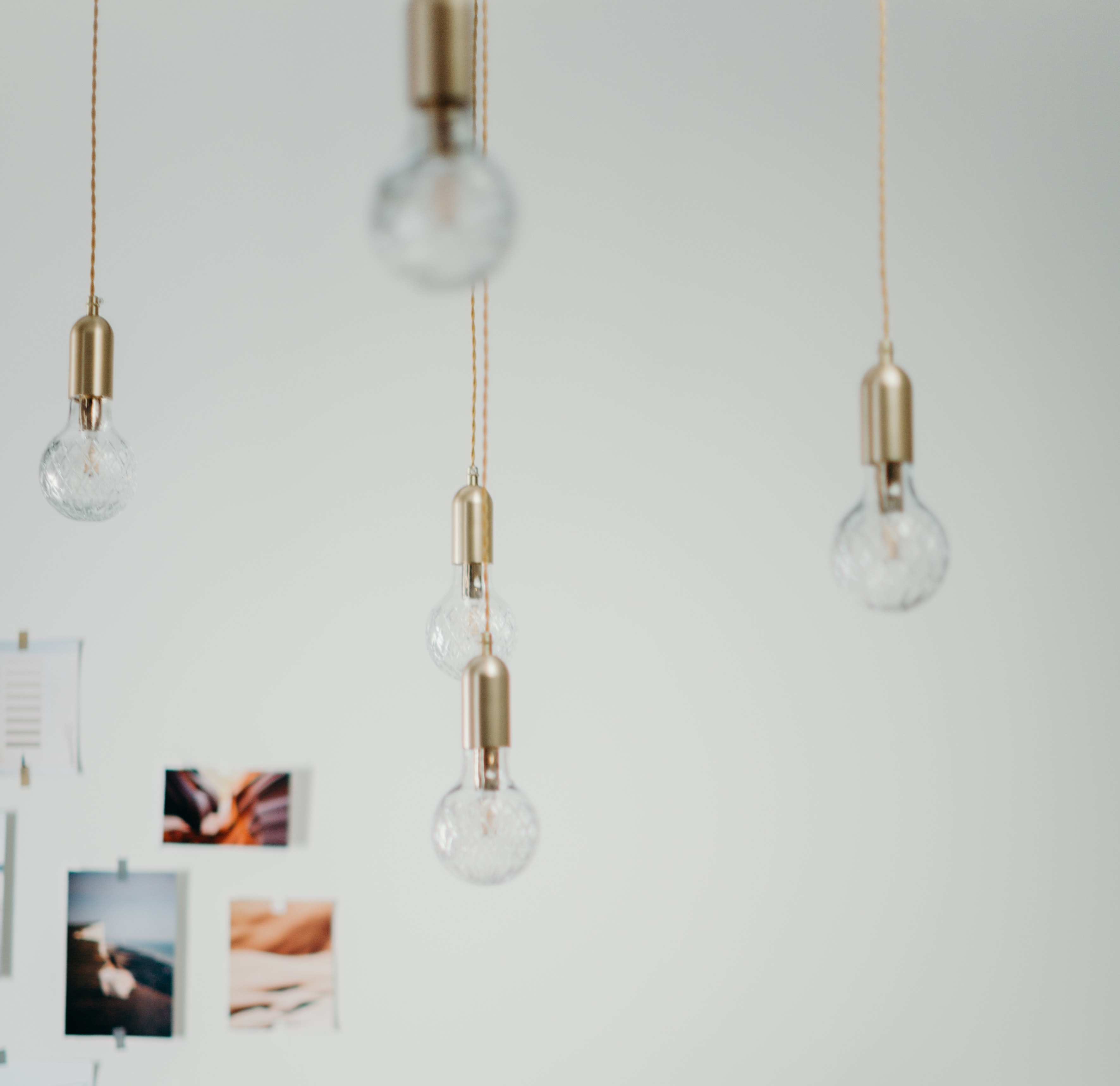 Lightbulbs with gold accents hang from the ceiling, as we look at a wall with images taped up, out of focus.
